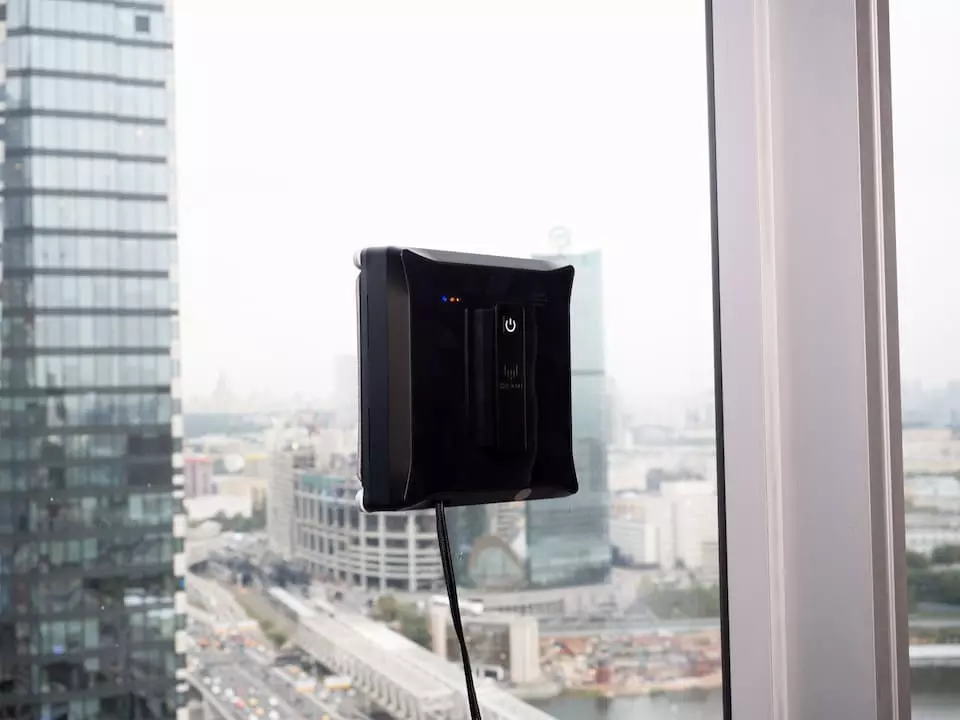 Моющий робот для окон Okami установлен на окне с видом на городской пейзаж